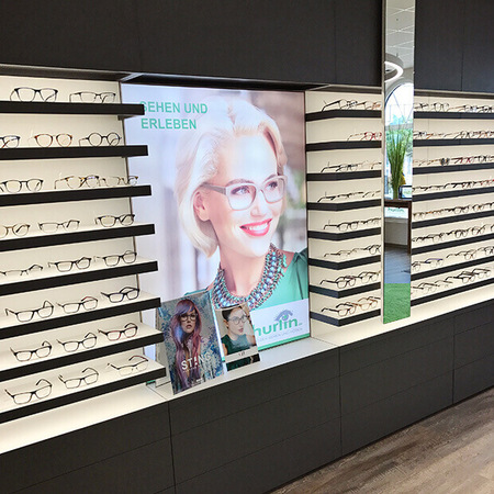Moderne Brillenauswahl in einem Optikergeschäft mit großer Brillenauslage und Werbung.